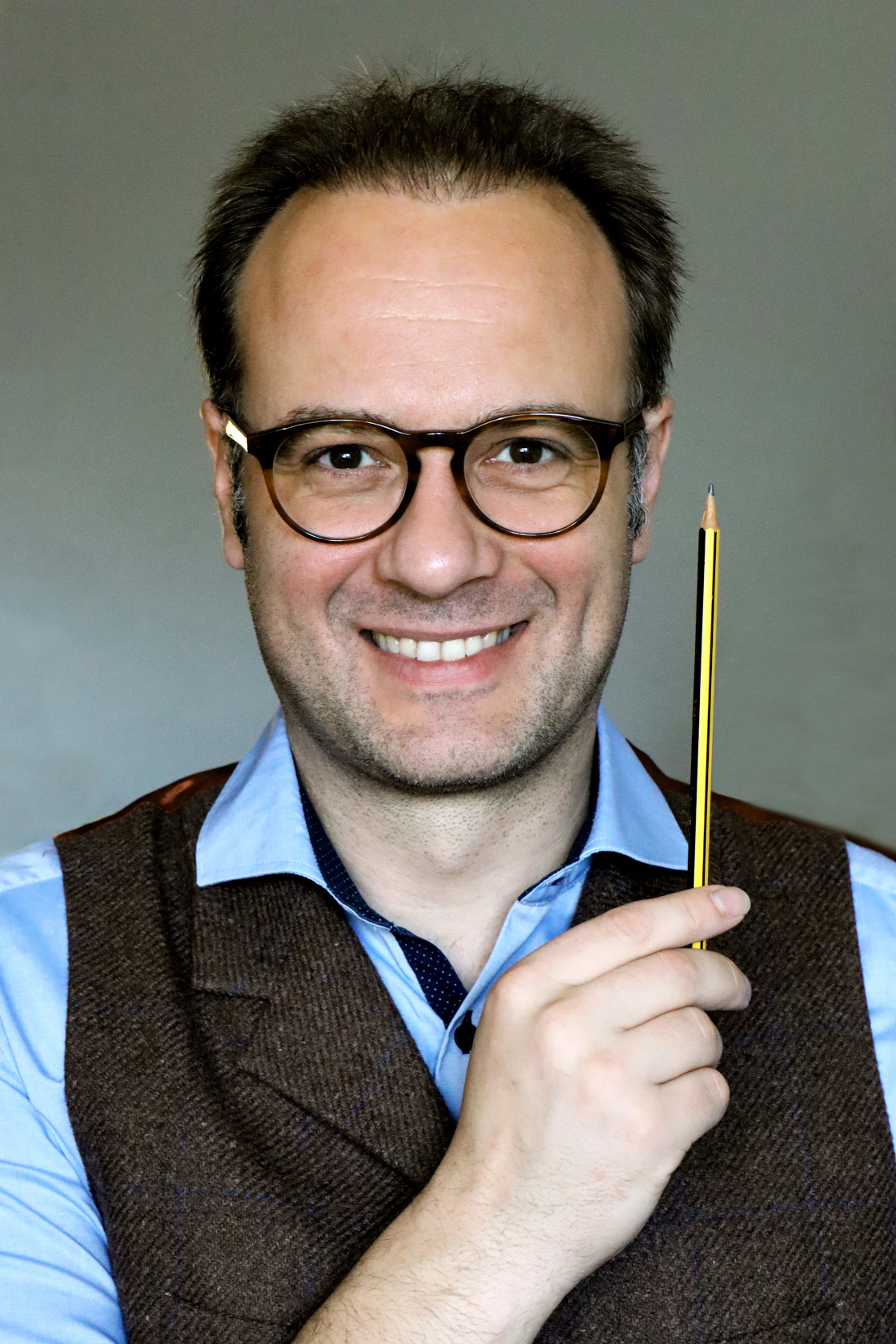 Mann mit Brille lächelt in die Kamera und hält einen Bleistift in der Hand